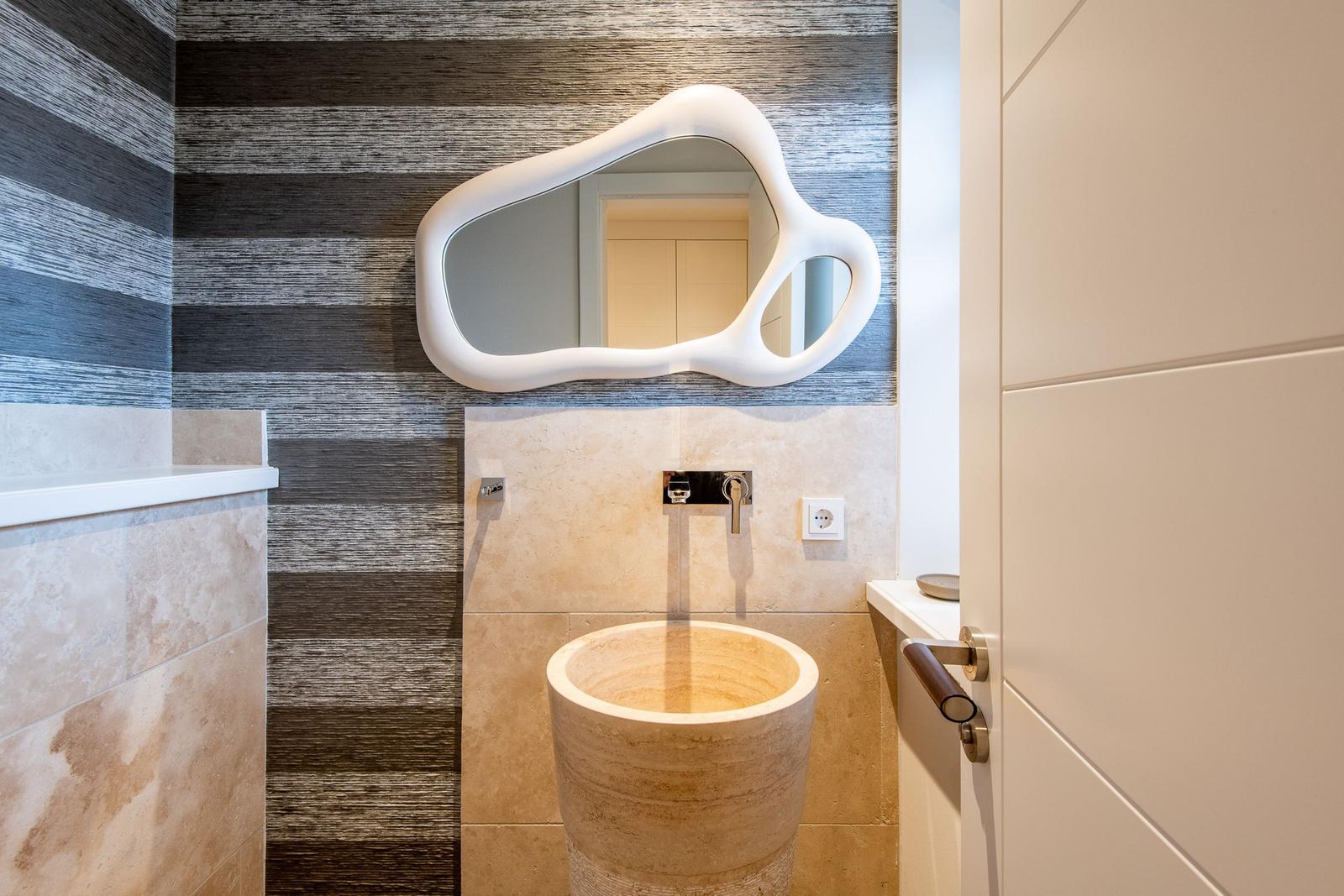 Bad mit Steinwaschbecken, Wandspiegel und Holzwandverkleidung.