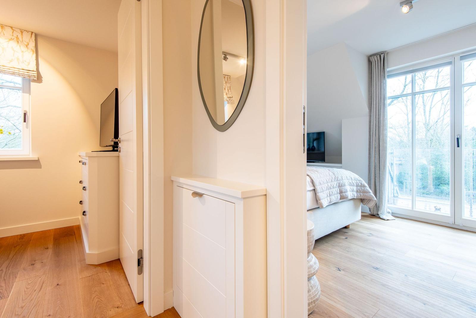 Schlafzimmer mit Bett und Fenster. Flur mit Spiegel und Schrank.