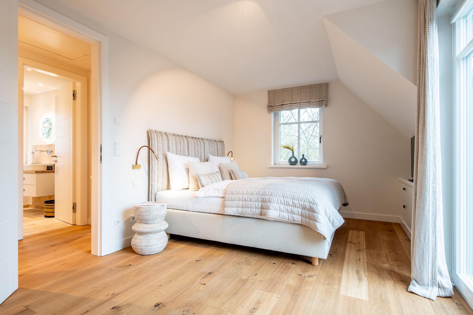 Schlafzimmer mit Bett, Fenster und angrenzender Badewanne.