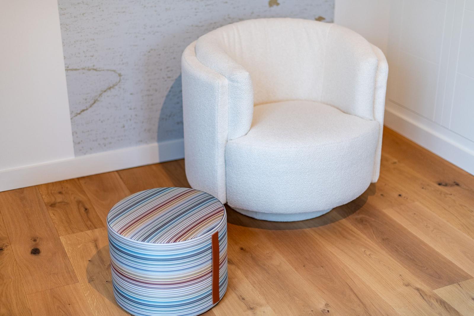 Runde weiße Sitzgelegenheit mit buntem Hocker auf Holzboden.