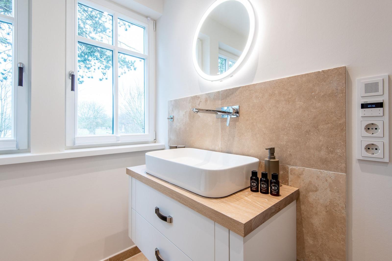 Badezimmer mit Waschbecken, Spiegel und Fenster. Holzoberfläche und Steinwand.