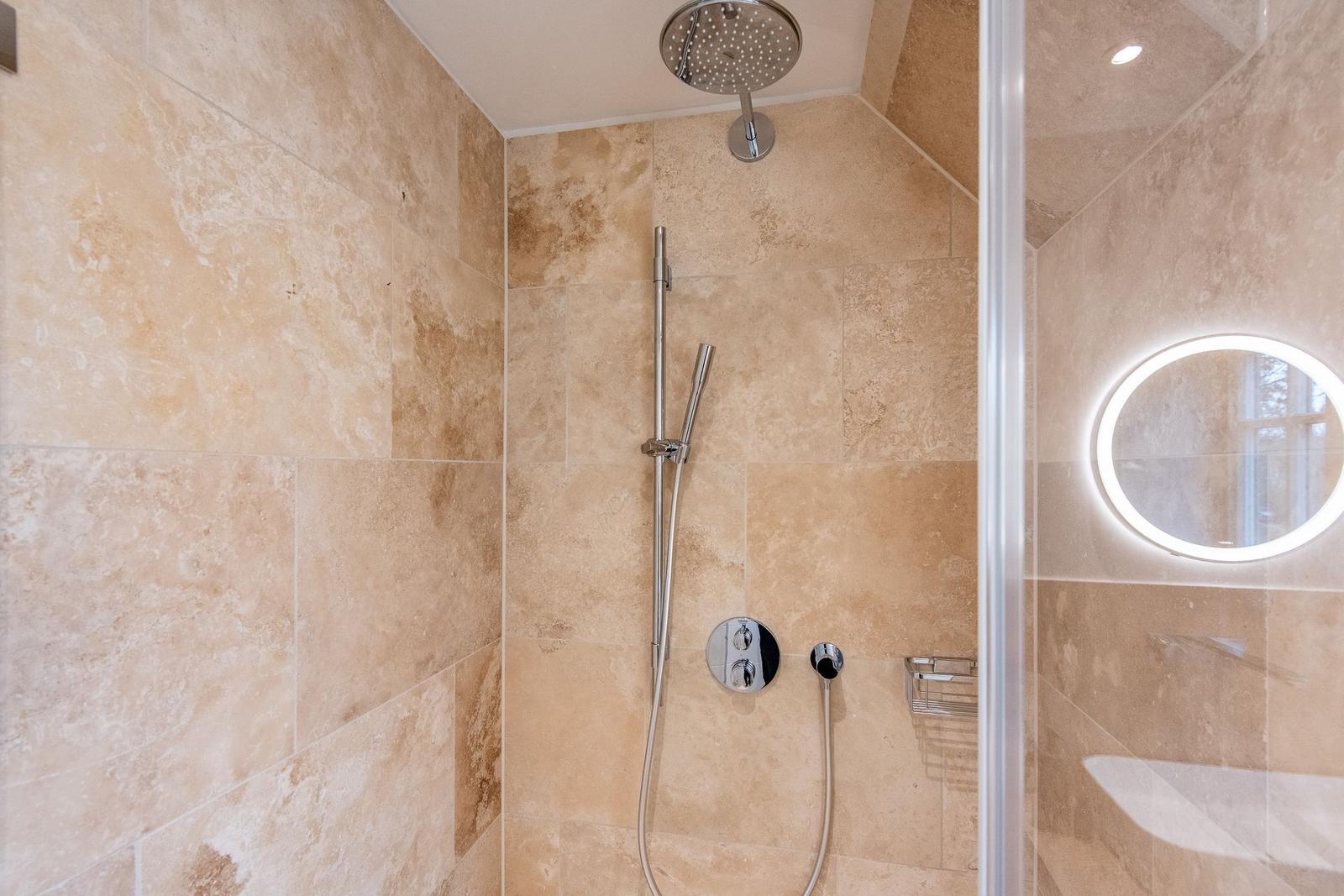 Duschkabine mit Duschbrause, Handdusche und runden Spiegel.