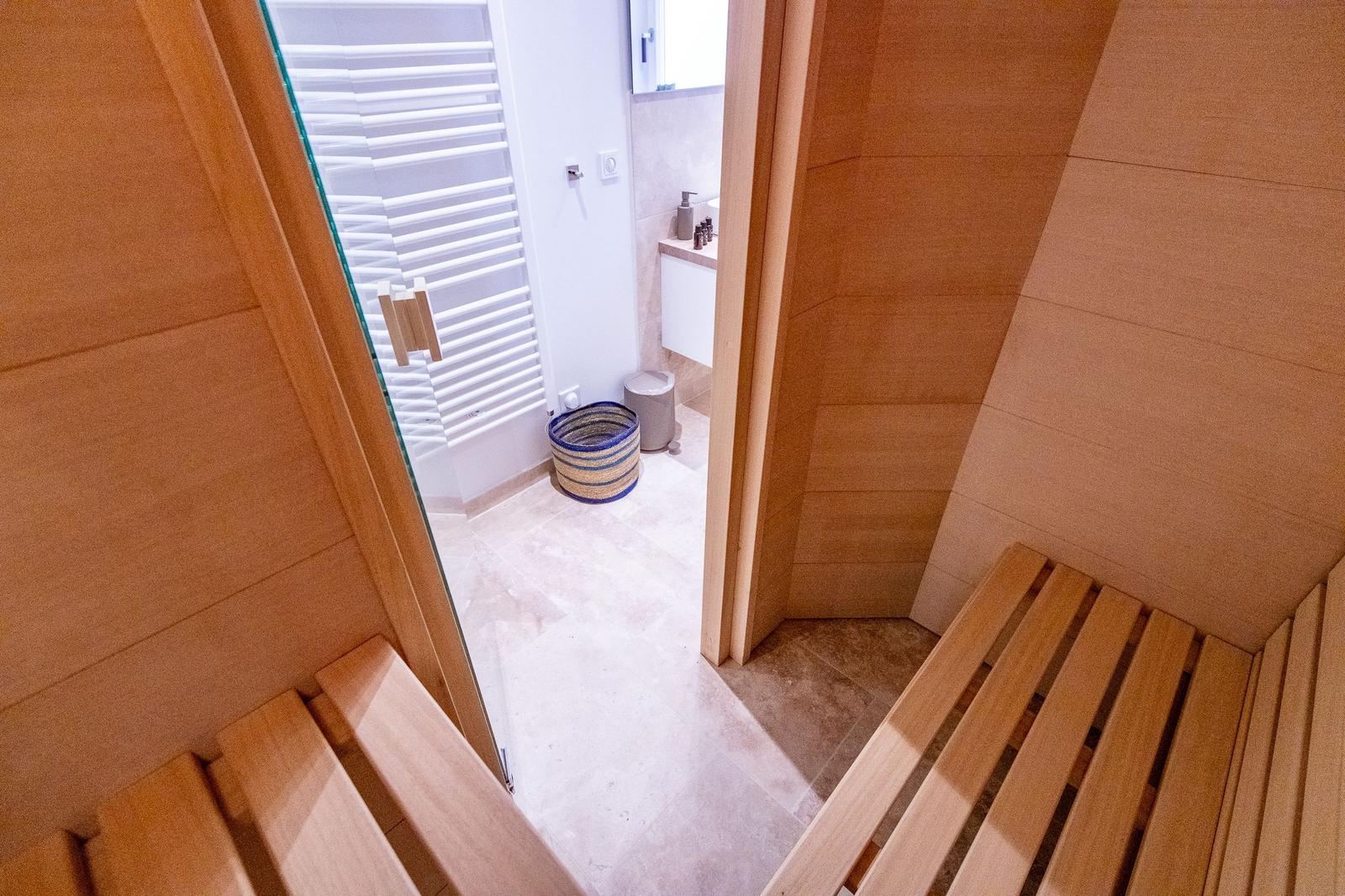 Sauna mit Holzbänken und Blick in das Badezimmer mit Dusche.