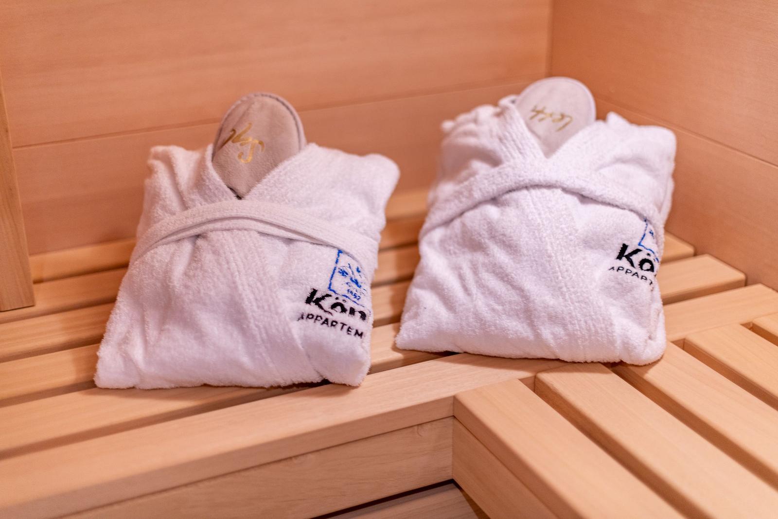 Zwei weiße Bademäntel mit Logo liegen auf Holzbank in Sauna.