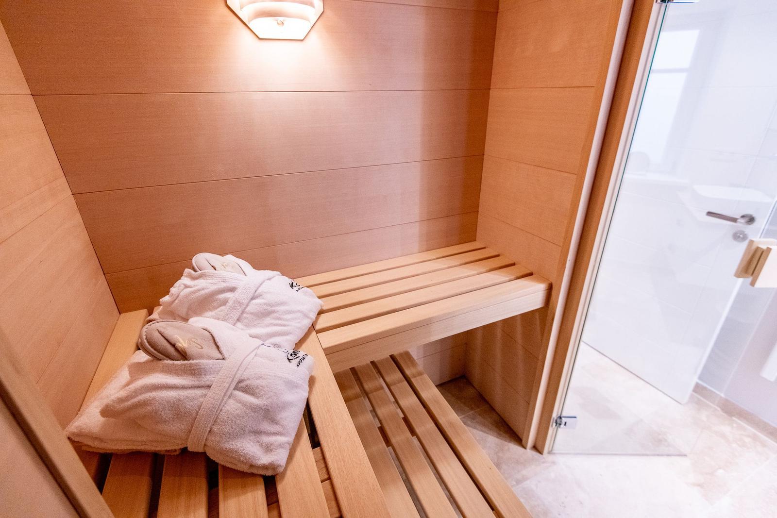 Sauna mit Holzbank und Bademantel. Tür führt in Duschbereich.