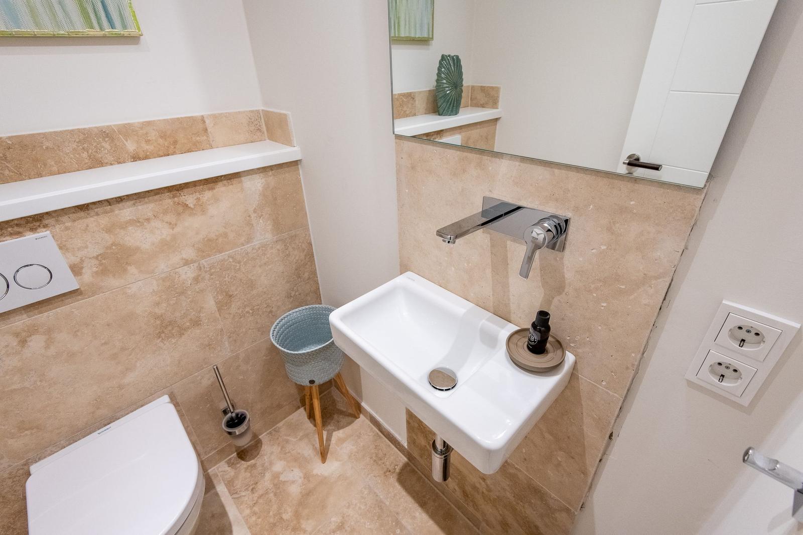 Badezimmer mit Waschbecken, Spiegel und Toilette.