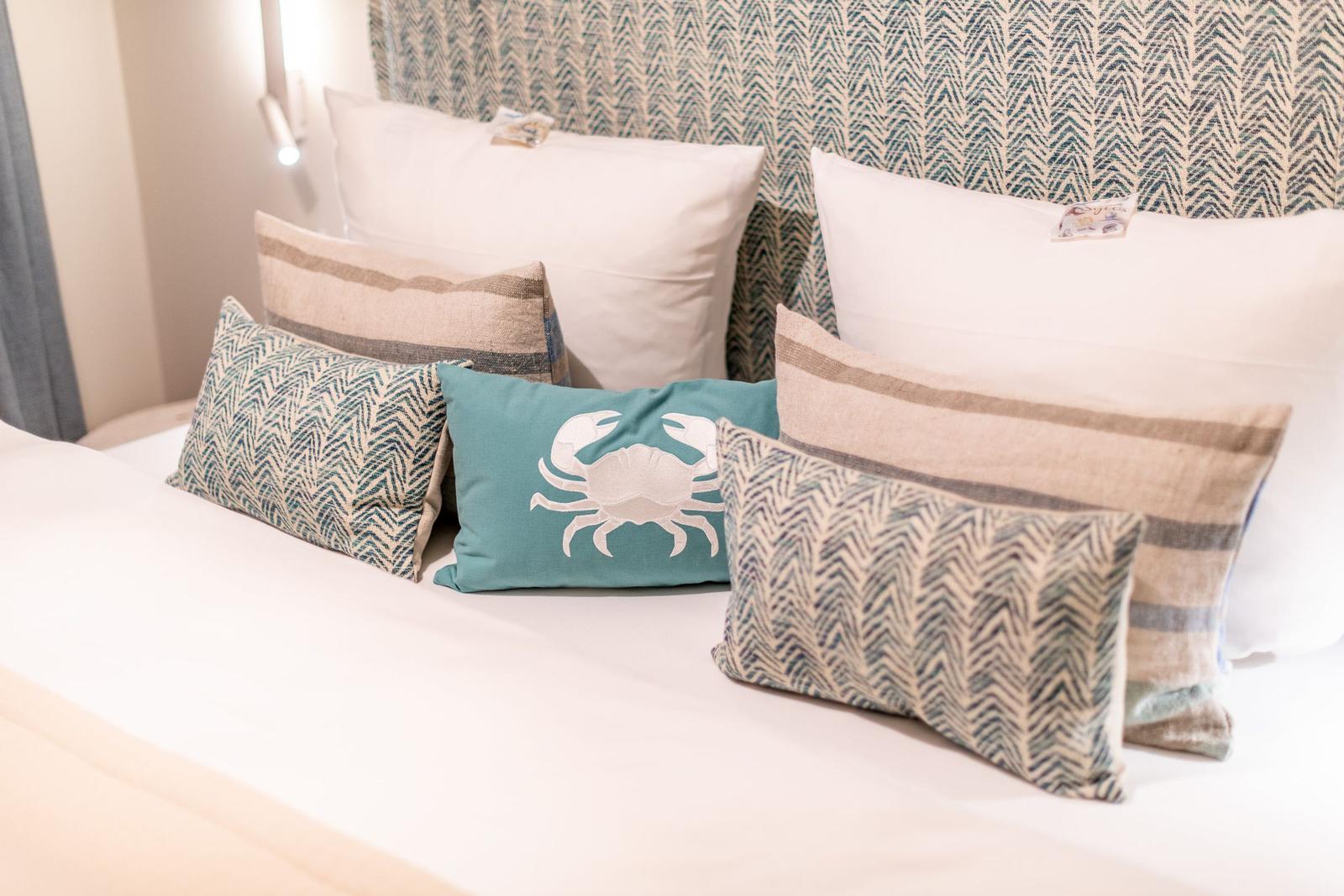 Bettkopfteil mit Muster, mehrere Kissen mit verschiedenen Mustern und einem Krabbenmotiv.