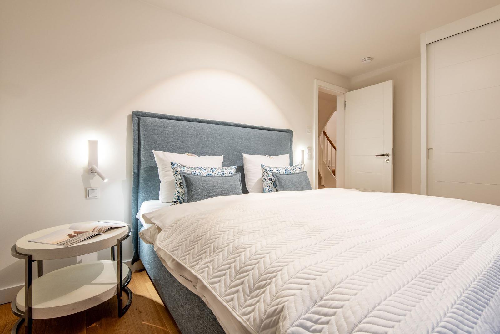 Schlafzimmer mit Bett, Nachttisch und Schrank. Hintergrund zeigt eine Treppe.