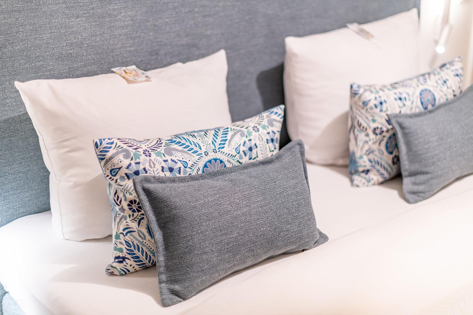Bettkopfteil mit Kissen in Grau, Weiß und Blau-Muster.