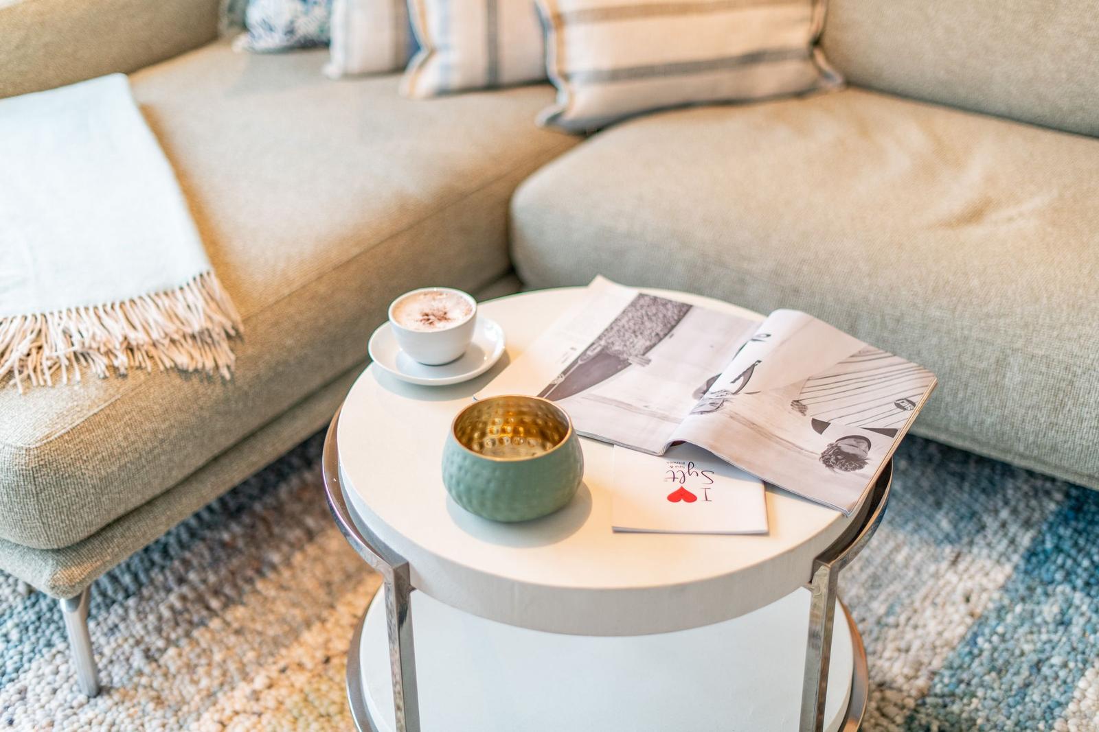 Runde Tisch mit Kaffeetasse, Zeitschrift und Schale vor einem Sofa.