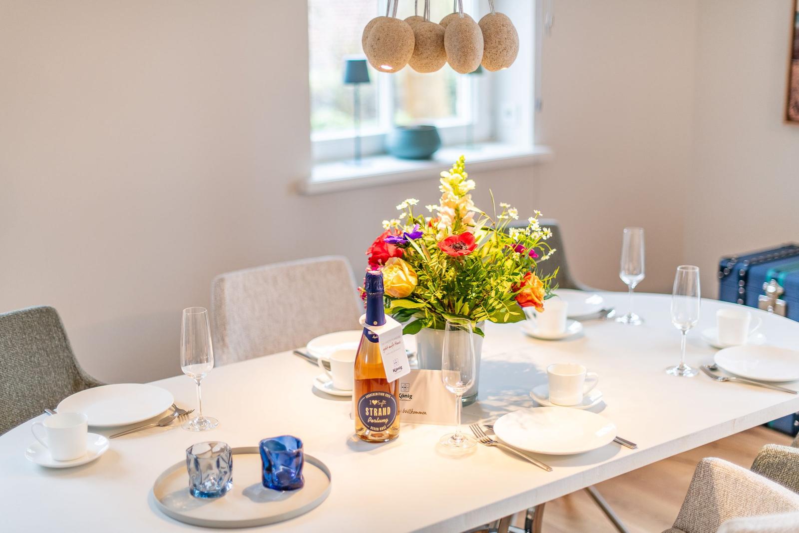 Tisch gedeckt mit Blumen, Gläsern und einer Flasche.