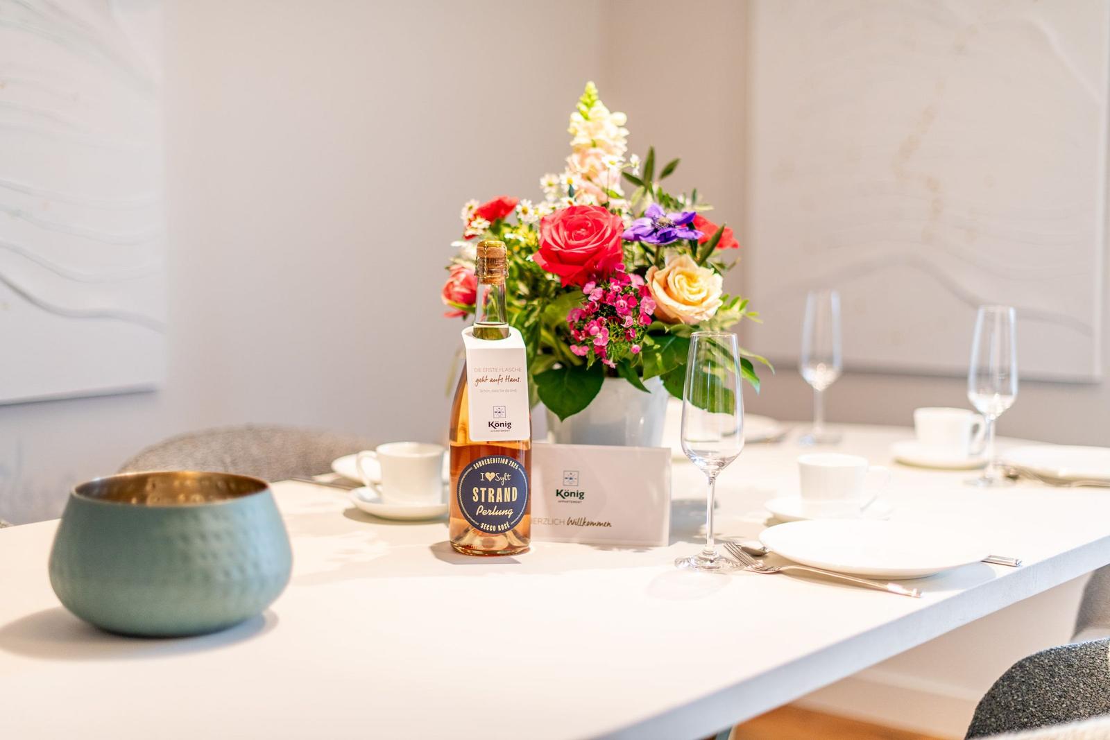 Tisch gedeckt mit Blumen, Wein und Geschirr.