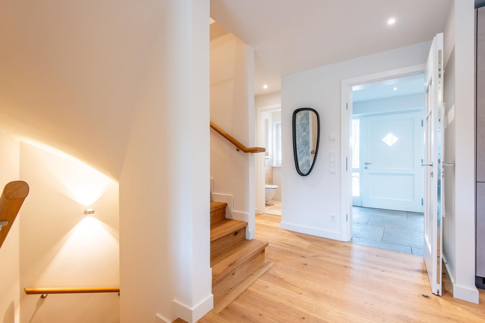 Eingangsbereich mit Holztreppe und Spiegel an der Wand.