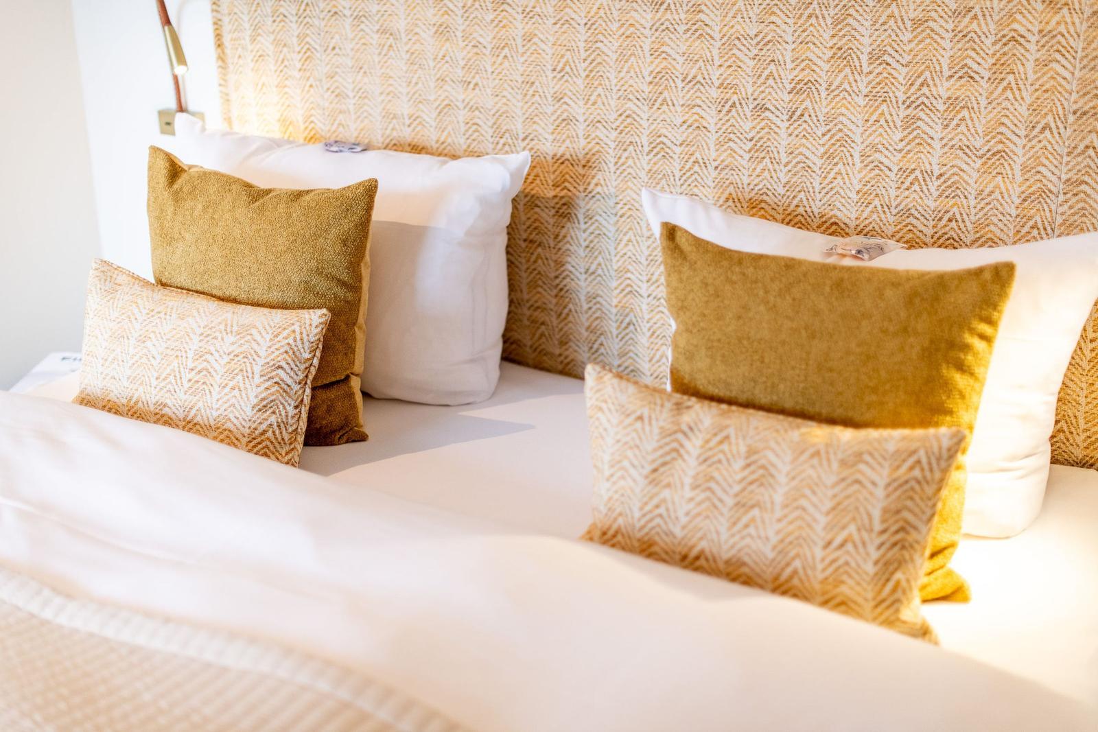 Bettkopfteil mit Muster, weiße Bettwäsche und gelbe Kissen