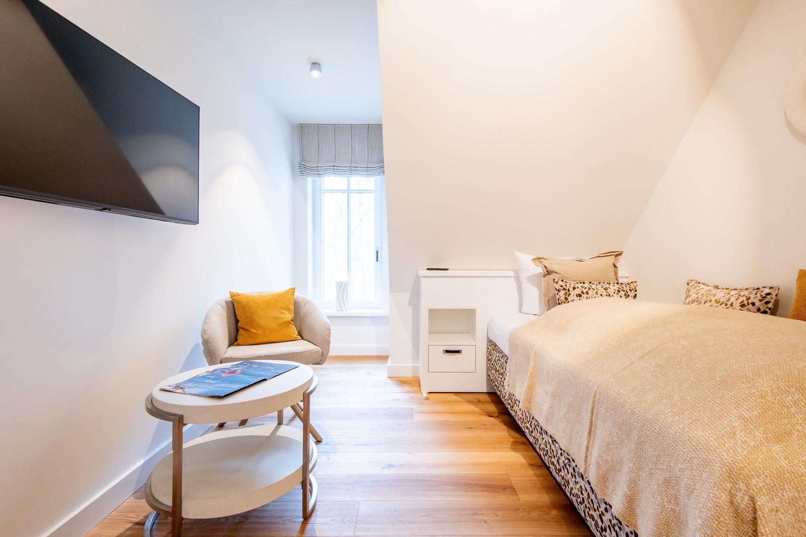 Schlafzimmer mit Bett, Nachttisch, Sessel und Fernseher an der Wand.