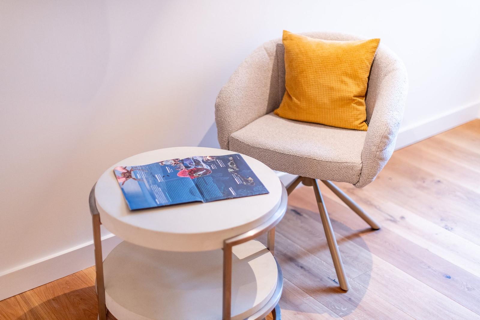 Ein Stuhl mit Kissen und Tisch mit Broschüre.