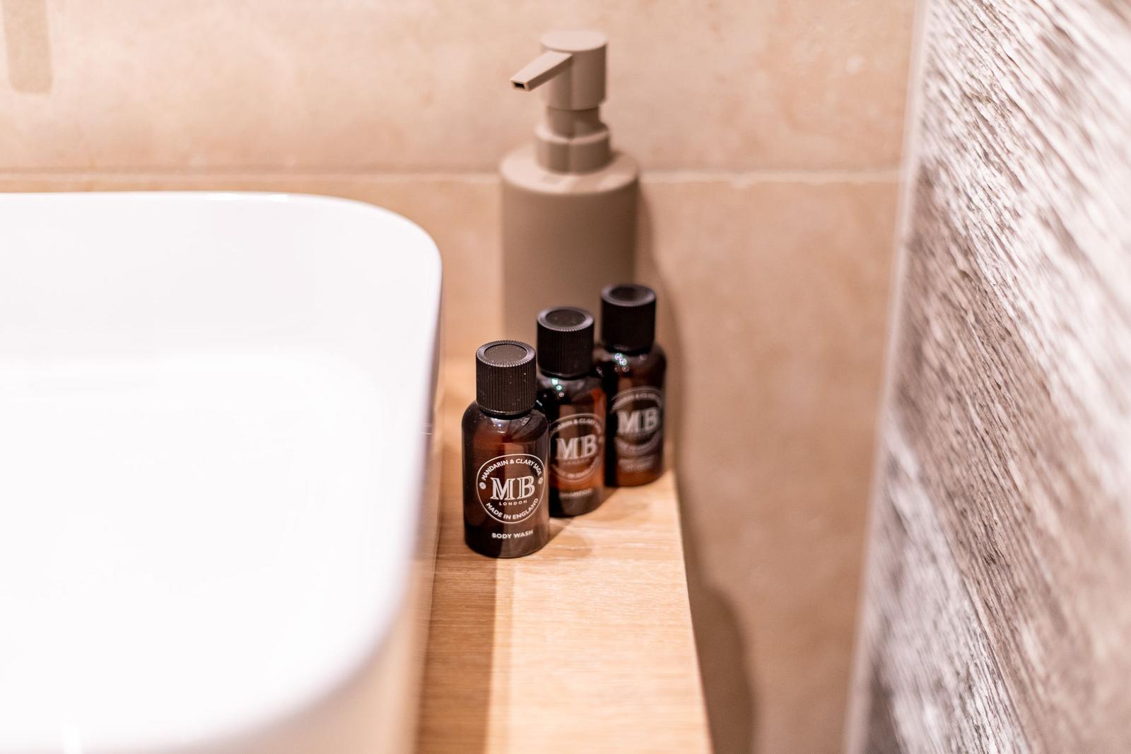 Badewanne mit Seifenspender und kleinen Flaschen auf Holzunterlage.