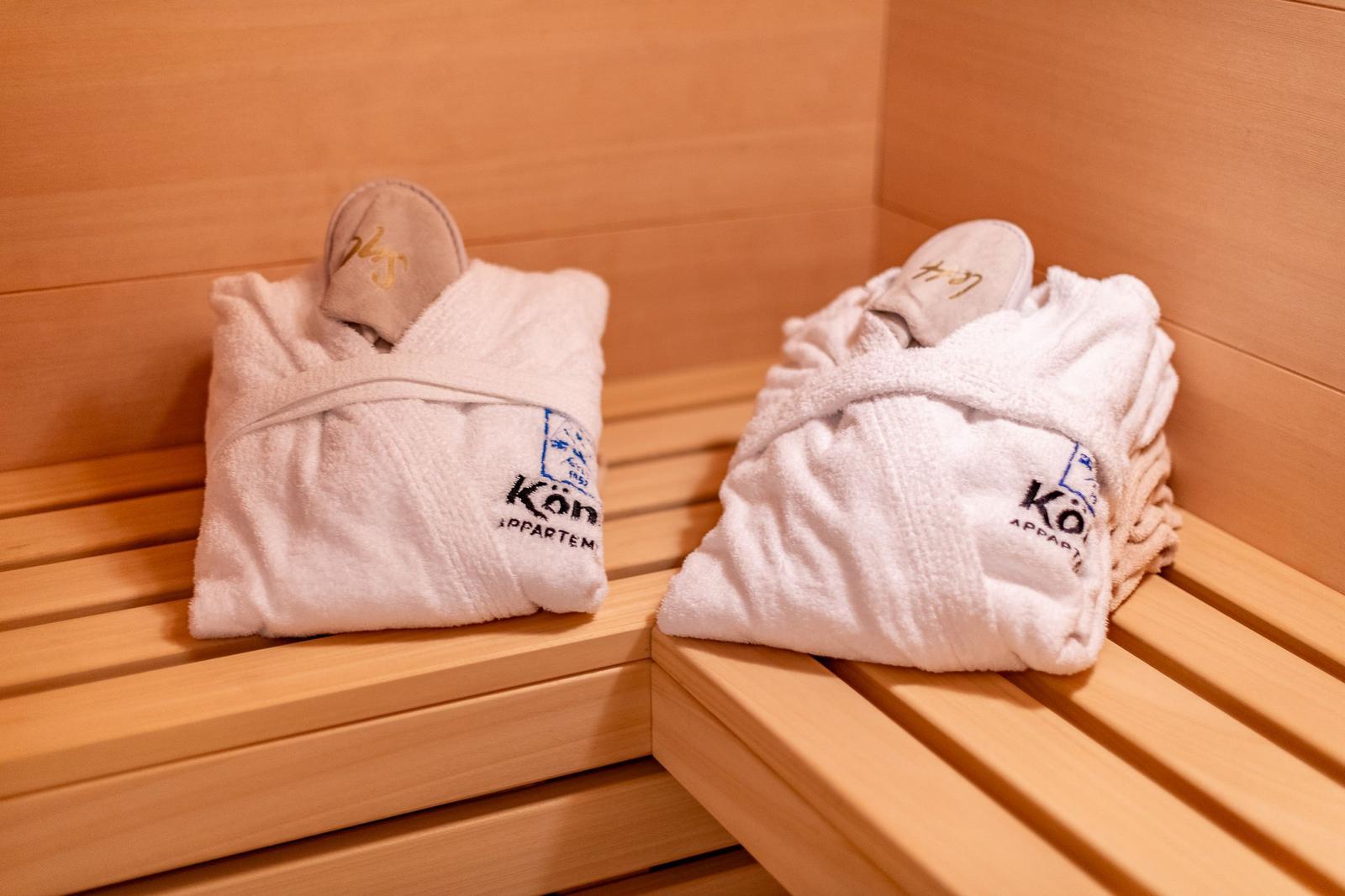 Zwei weiße Bademäntel mit Mützen liegen auf Holzbänken in einer Sauna.