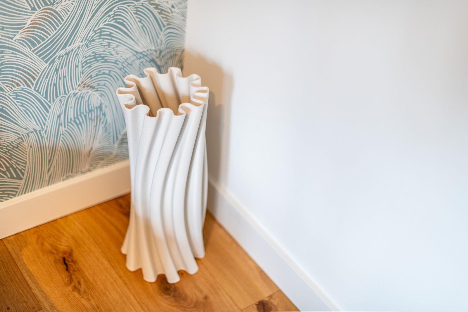 Weißer, wellenförmiger Vasenständer an der Wand mit gemustertem Tapetenabschnitt.