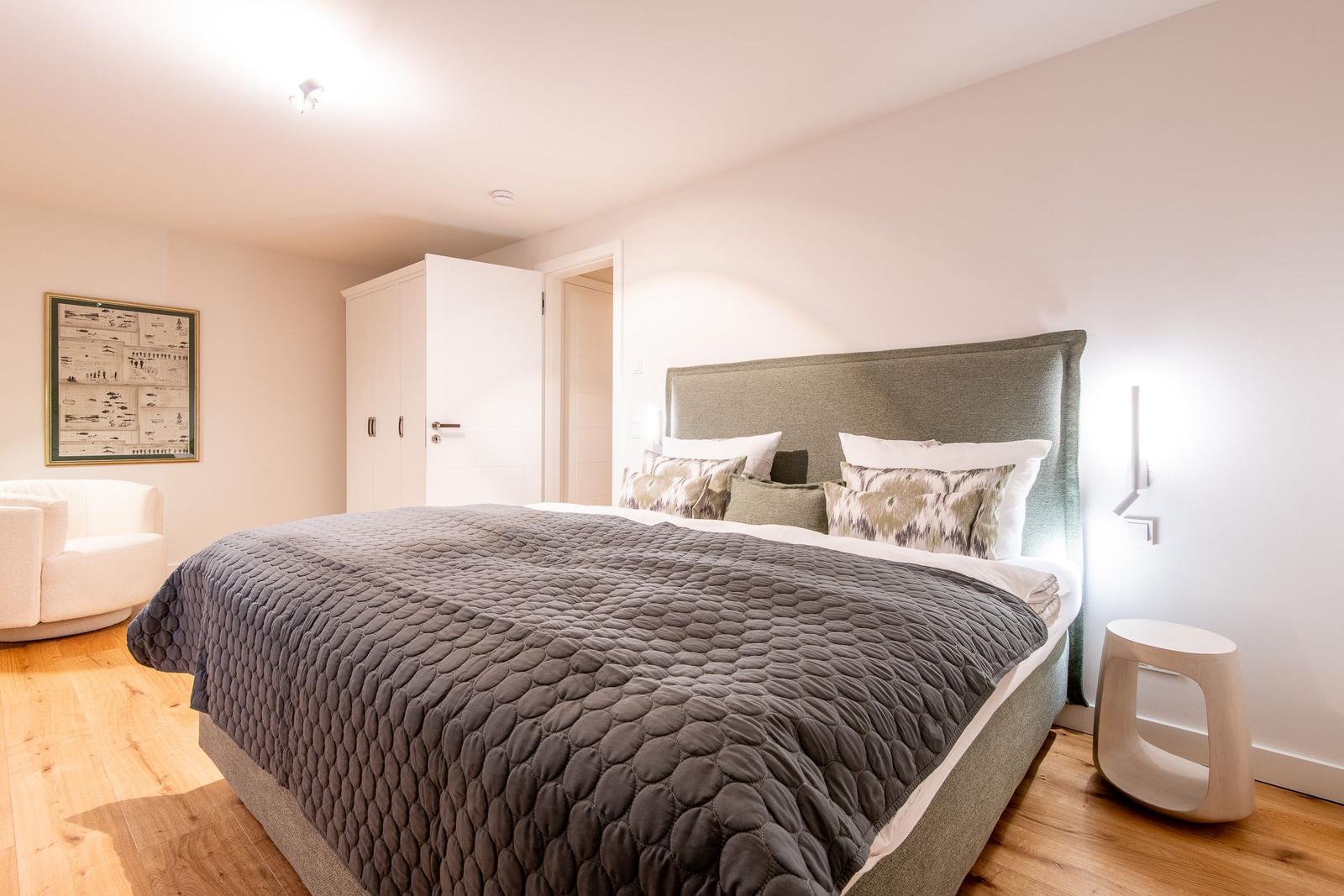 Schlafzimmer mit Bett, Kleiderschrank und Sitzgelegenheit.