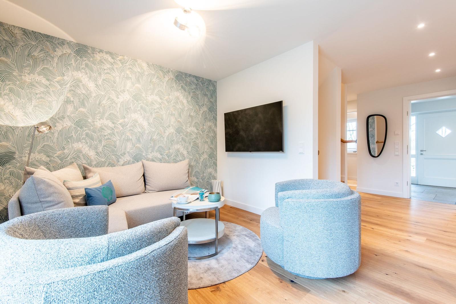 Wohnzimmer mit Sofa, zwei Sesseln und Wandbild. Fernseher an der Wand.