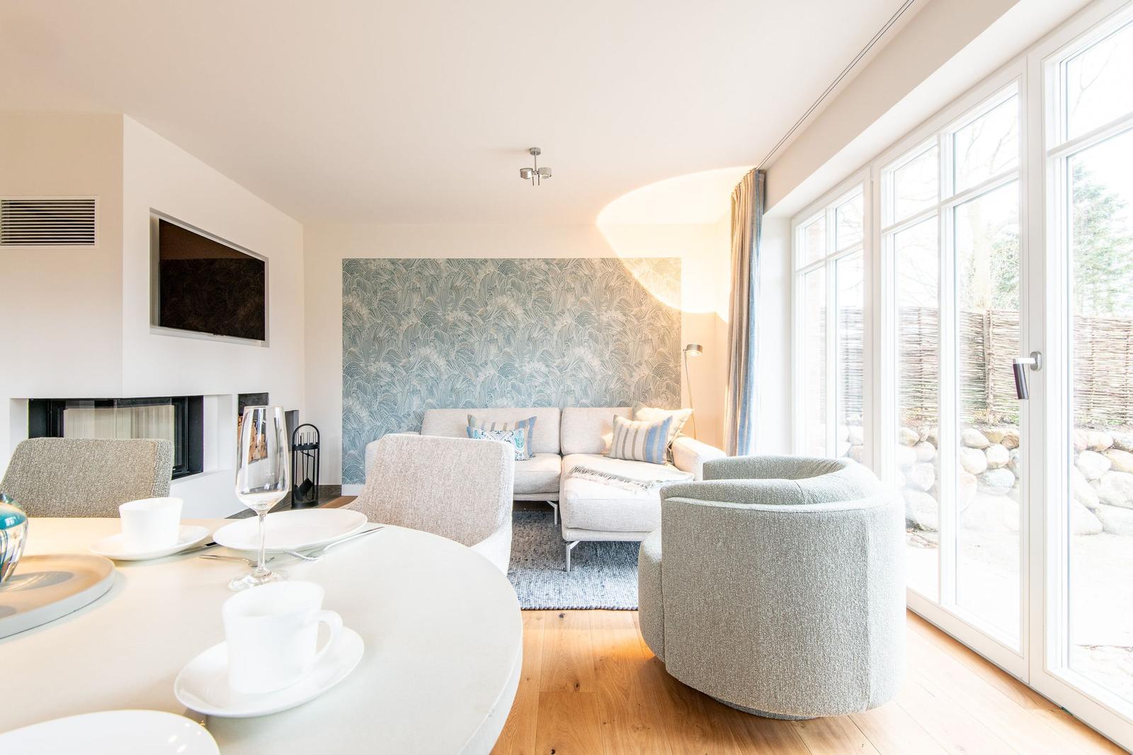 Wohn- und Essbereich mit Sofa, runden Sessel und großem Fenster. Wand mit Muster. Esstisch mit Geschirr.