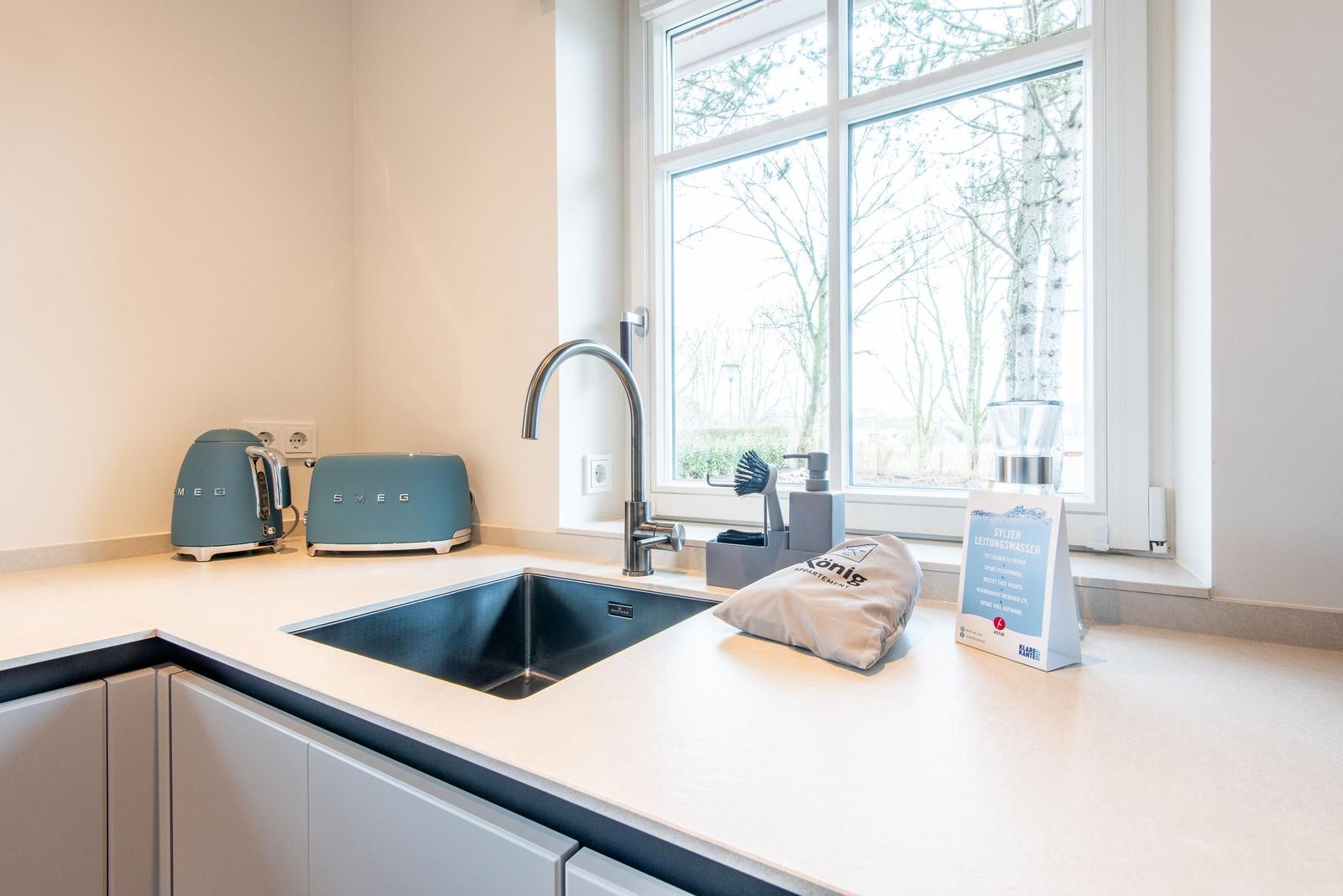 Küche mit Waschbecken, Fenster und Küchengeräten.