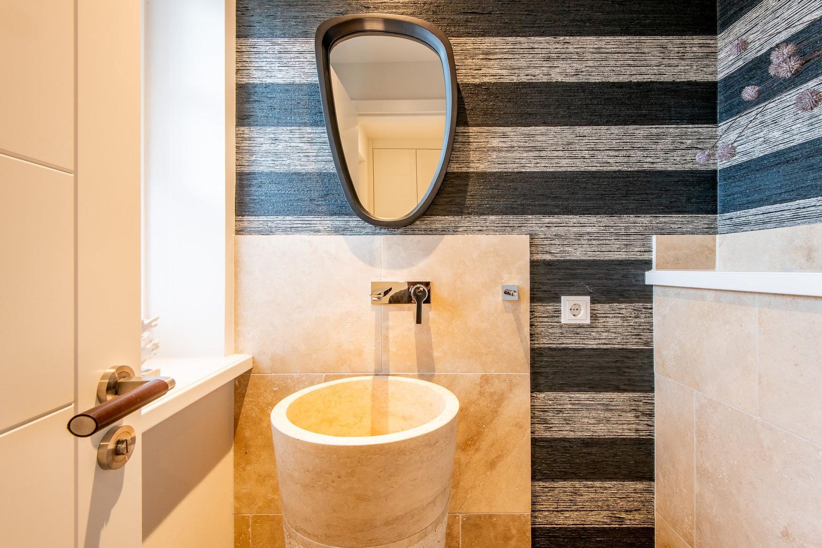 Bad mit Steinspüle, Wandspiegel und gestreifter Tapete.