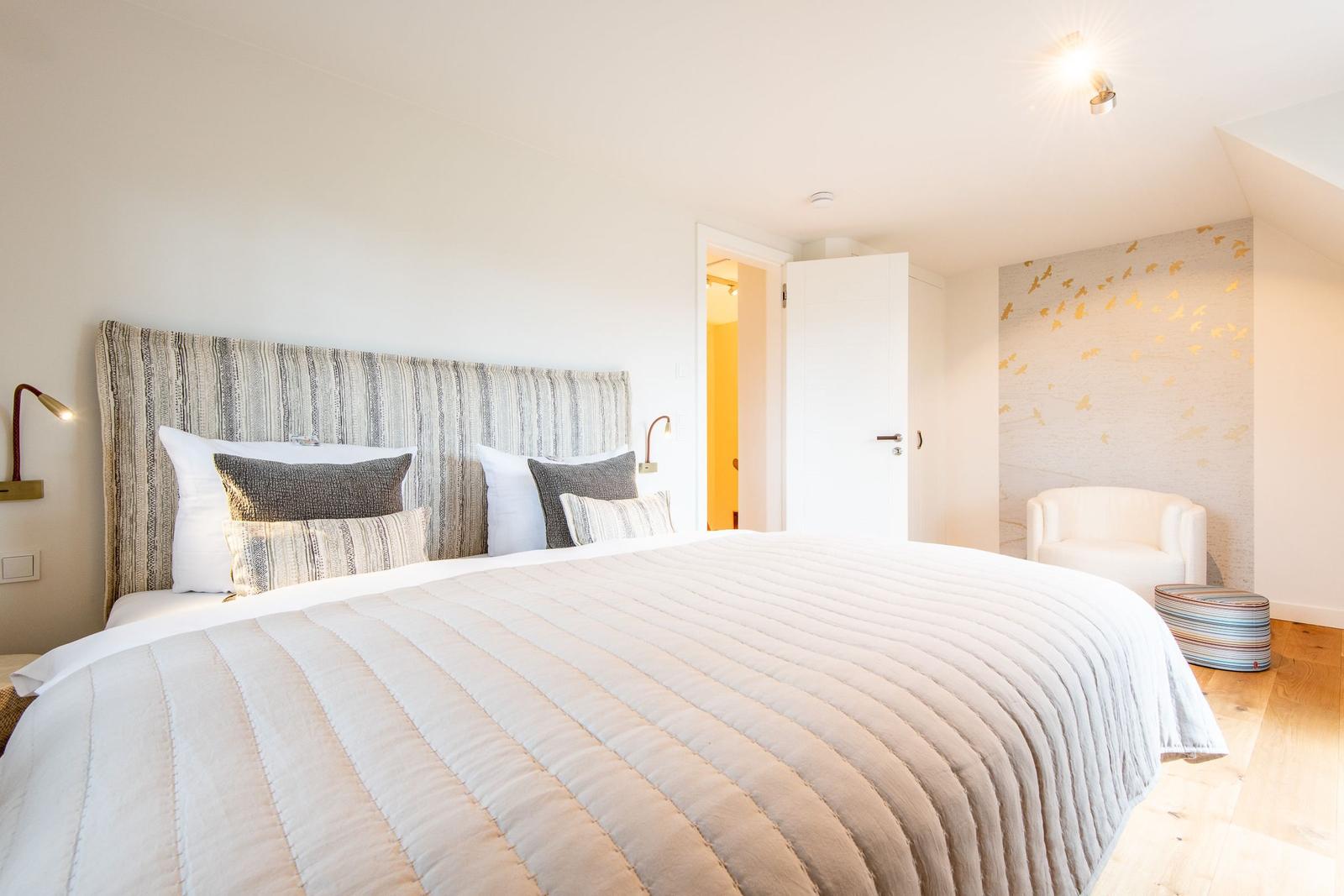 Schlafzimmer mit großem Bett, Wand mit goldener Verzierung und Sitzgelegenheit.