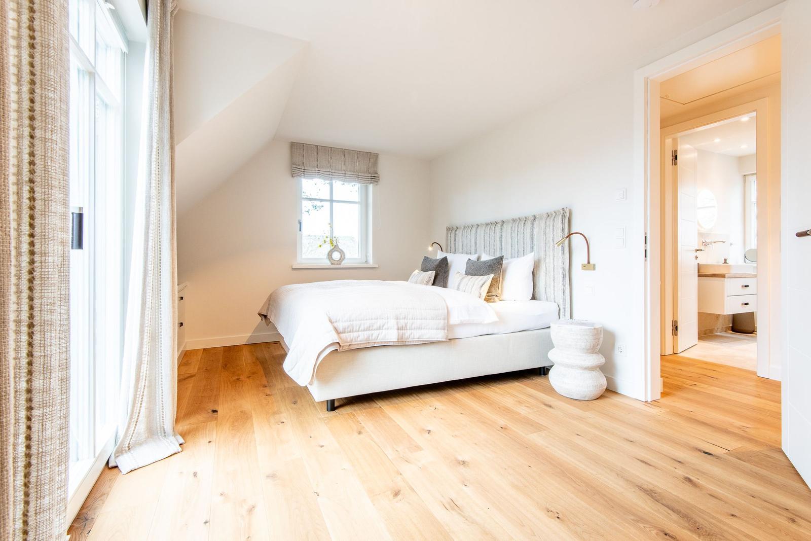 Schlafzimmer mit Dachschrägen, Holzboden und Blick in das Bad.