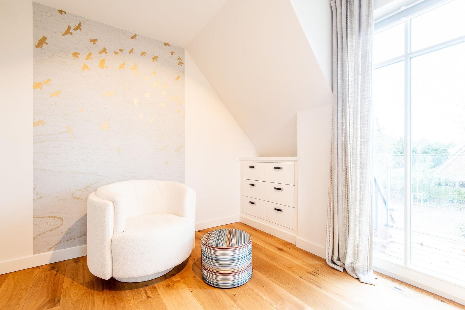 Zimmer mit weißer Sitzgelegenheit, Holzboden und großem Fenster.