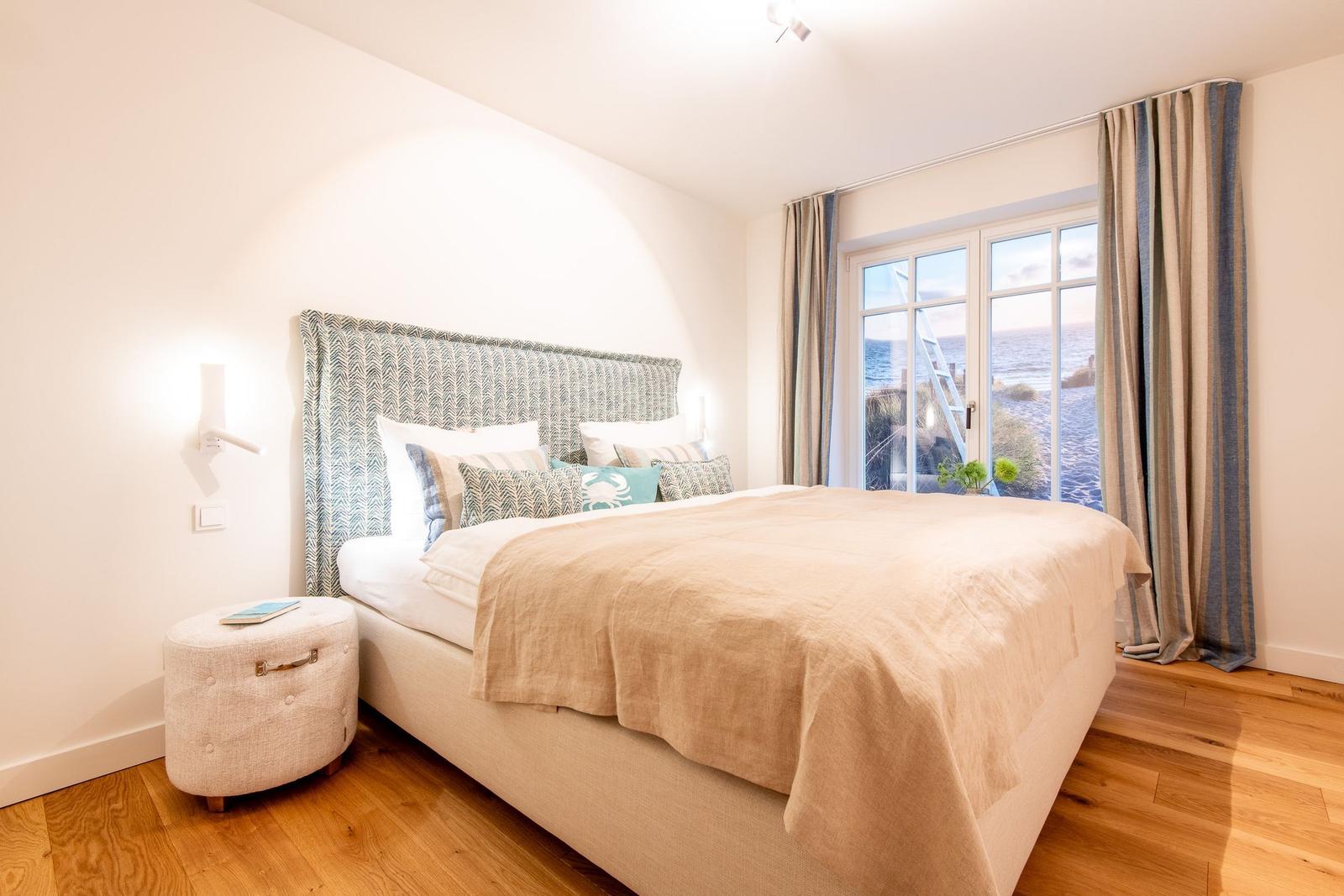 Schlafzimmer mit Blick aufs Meer. Bett, Fenster und Holzboden.