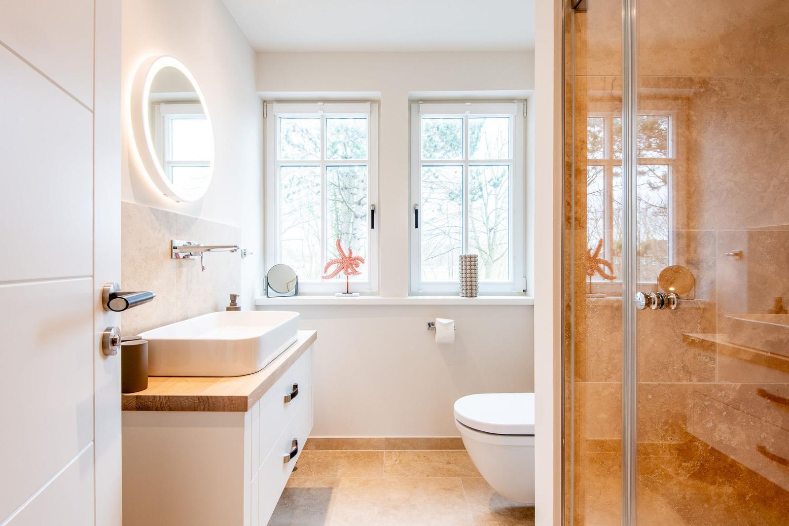 Badezimmer mit Dusche, Waschbecken und Toilette. Fenster mit Blick auf Bäume.