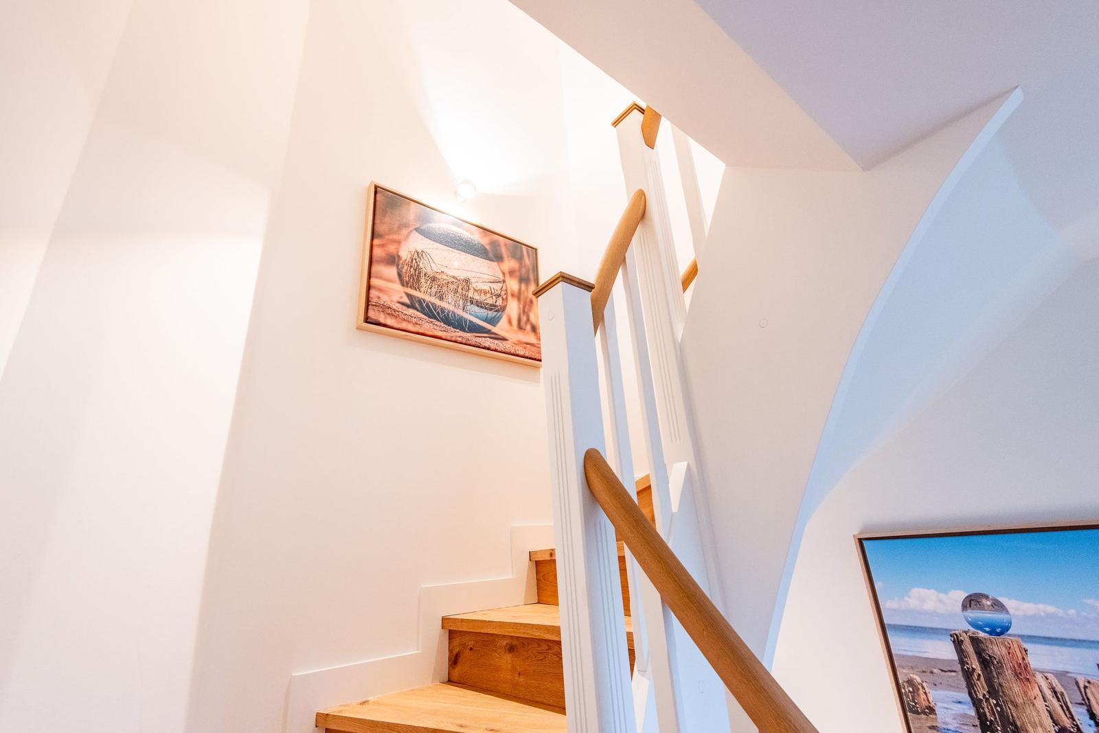 Helle Treppe mit Holzstufen und Bildern an den Wänden.