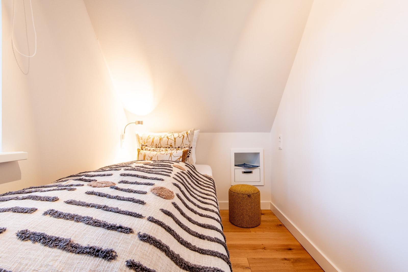 Schlafzimmer mit Bett, Nachttisch und Stuhl unter schrägen Wänden.