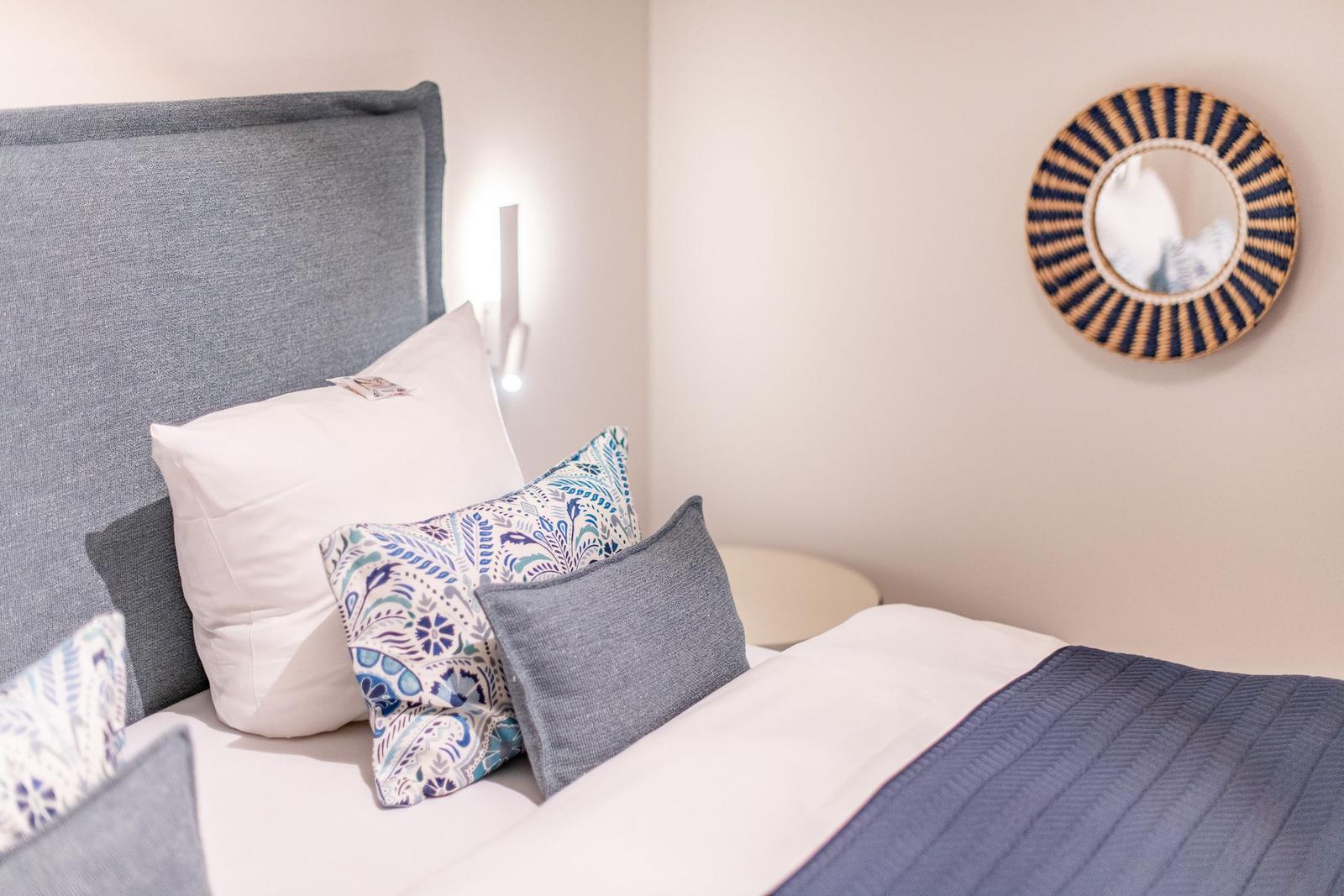 Ein Bett mit Kissen und einer Decke, Wandspiegel und Nachttisch