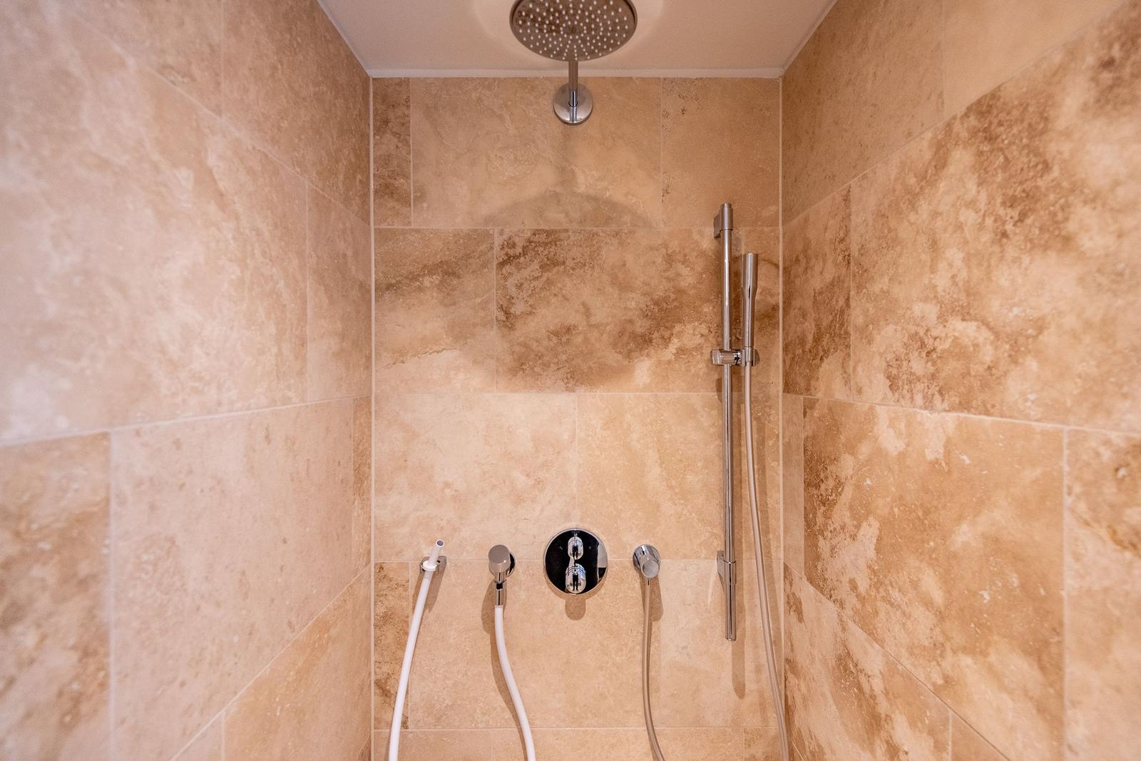 Dusche mit Duschbrause, Handbrause und Duschstange an Steinwand