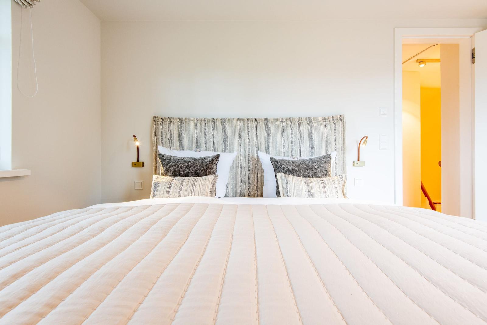 Ein Bett mit gestreifter Matratze und Kopfkissen. An den Wänden hängen Wandlampen.