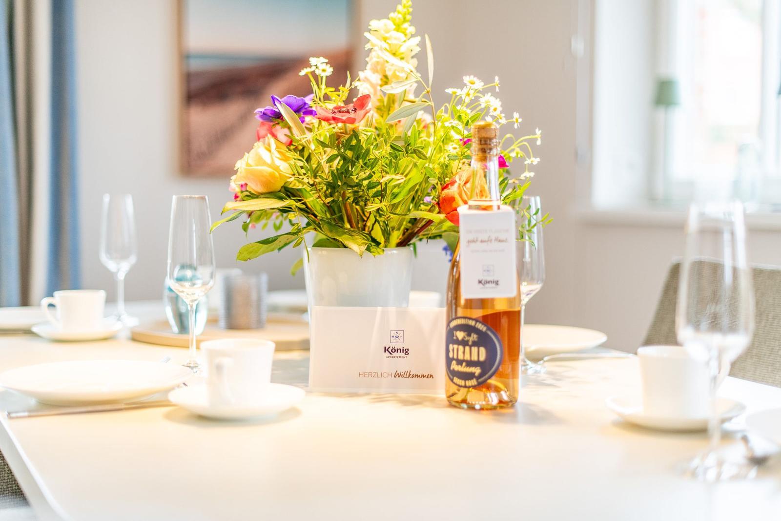 Tisch mit Blumen, Gläsern und einer Flasche Willkommensgetränk.