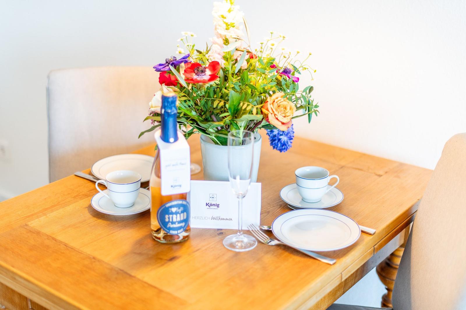 Holztisch mit Blumenvase, Gläsern und Tassen für zwei Personen.