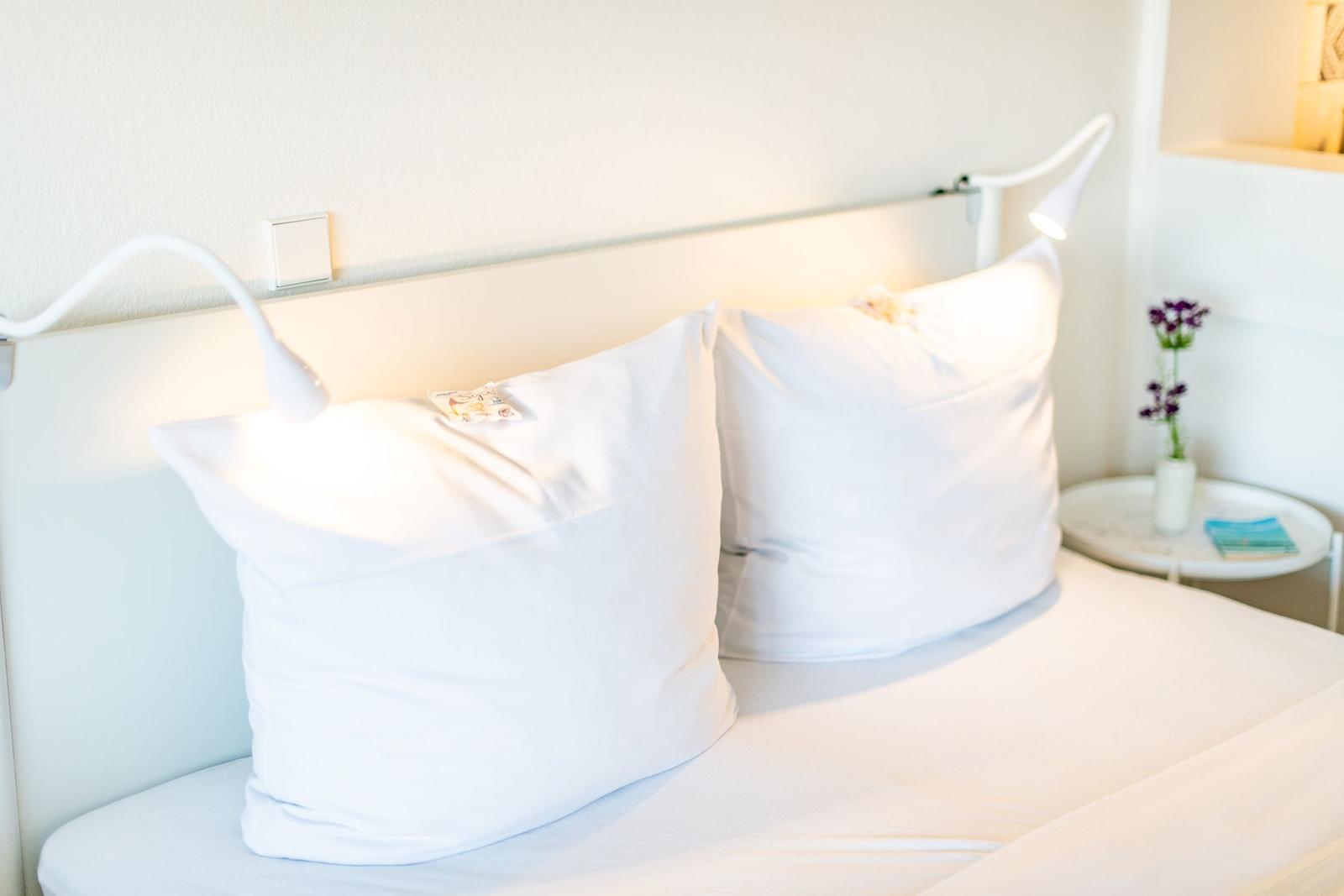 Ein Bett mit weißen Kissen und Nachttisch mit Blumen.