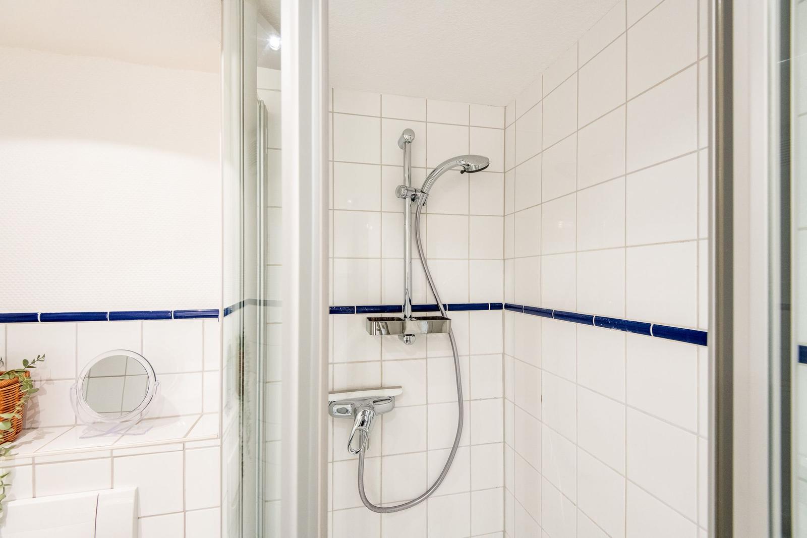 Dusche mit Duschbrause und blauer Zierleiste an den Wänden.