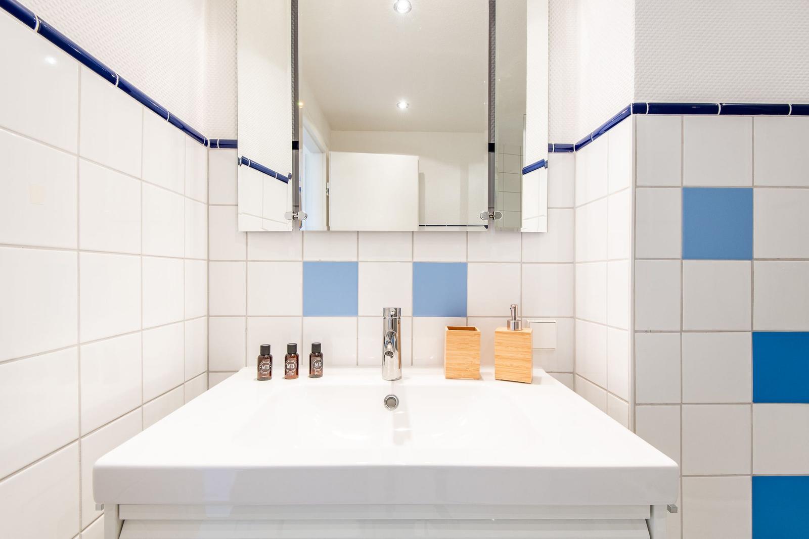 Bad mit weißen Fliesen und blauen Akzenten, Waschbecken und Spiegel.