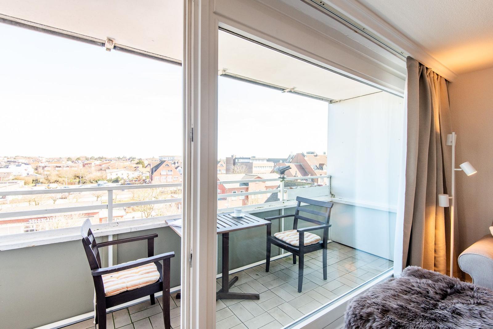 Balkon mit Tisch und zwei Stühlen, Blick auf Wohngebiet.