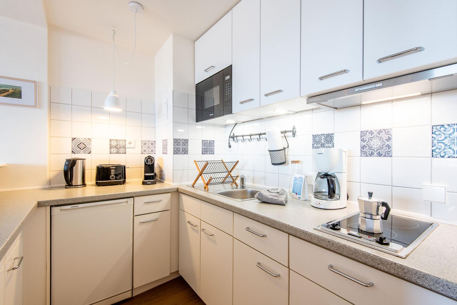 Küche mit weißen Schränken, Spüle, Herd und Kühlschrank.