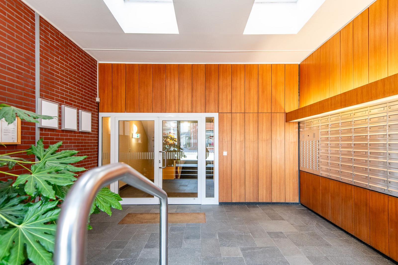 Hauseingang mit Holzwand, Briefkastenreihe und Glasfronttür.