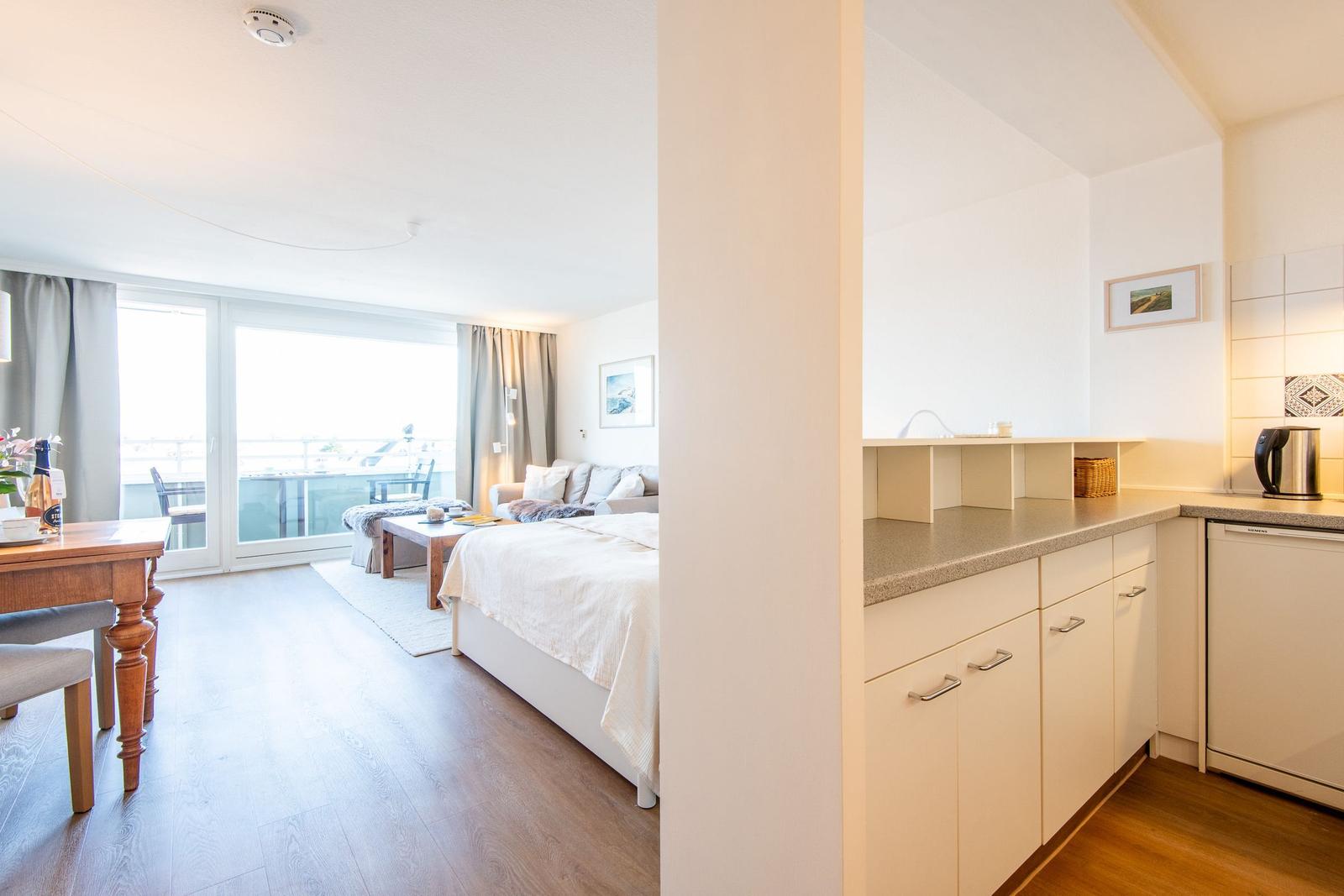 Wohnung mit Küche, Schlafzimmer und Balkon. Holzfußboden und weiße Möbel.