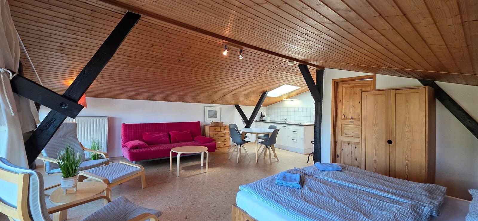 Doppelbett, Sofa, Tisch und Stühle in einem Raum mit Holzdecke und Balken.