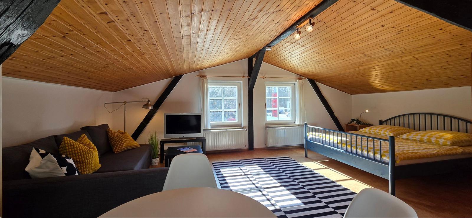 Ein Schlafzimmer mit Dachschrägen, Bett, Sofa und Fernseher.