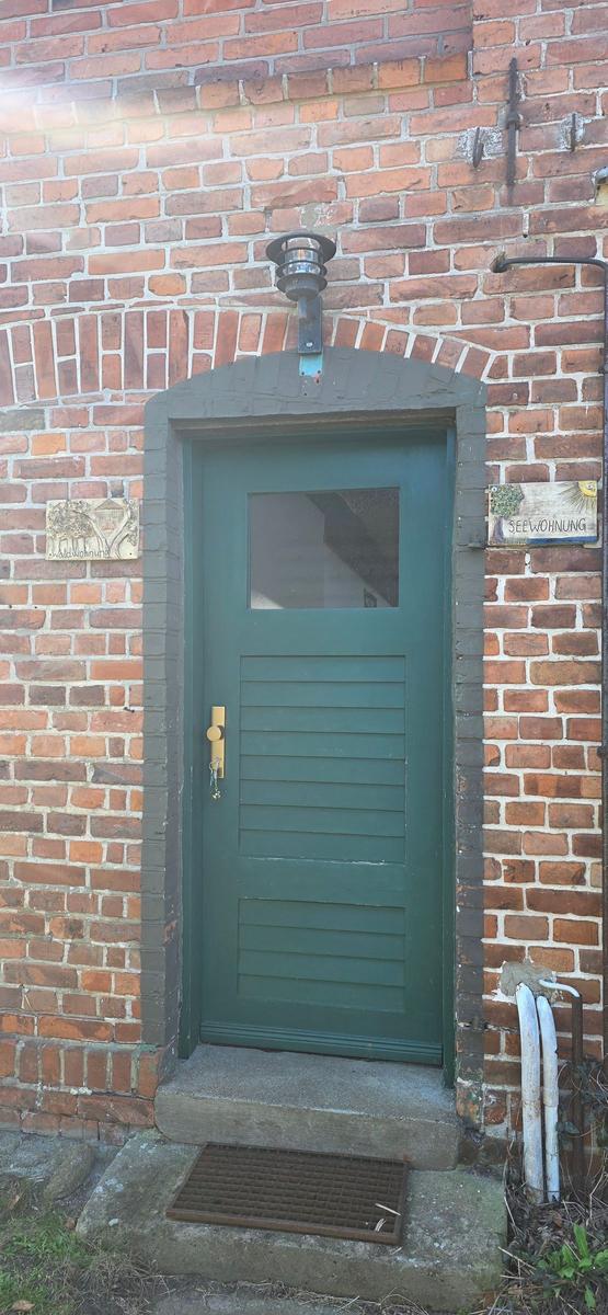 Grüne Haustür mit Glasfenster in rotem Ziegelhaus. Schilder an der Wand.